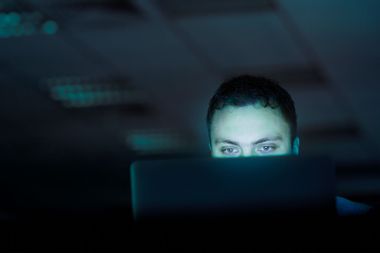 Man looking at the computer in a dark room