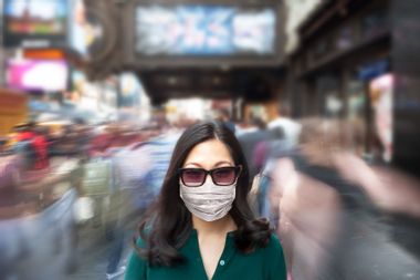 Woman wearing a surgical mask as crowd of people walk past her in blur motion