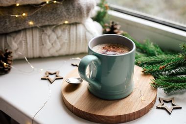 Cozy home picture of blue ceramic cup with coffee on window sill, Christmas decorations, warm knitted sweaters and pine tree green branches