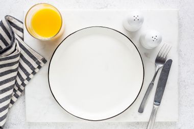 Empty plate, cutlery, orange juice and salt and pepper shaker table setting