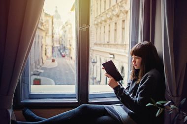 Young teenage girl reading by the window