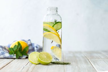 Bottle of infused water with a slice of lemon, cucumber and rosemary leaf in it.