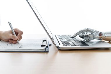 Robot hand using laptop and man hand writing