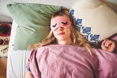 A young woman lying in bed and wearing a sleep mask
