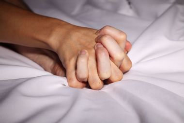 Couple in bed holding hands passionately