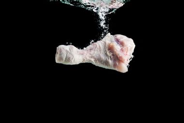 Chicken leg falls into the water on a black background