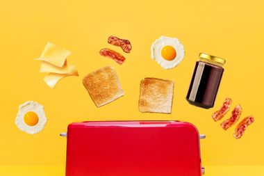 Toast popping out of a toaster alongside bacon, eggs, cheese and jelly