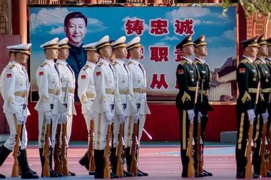 Military personnel stand in formation next to a portrait of China's President Xi Jinping