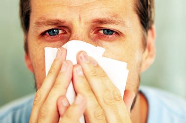 Red eyed man holding tissue to his nose