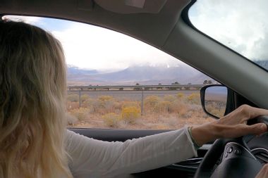 Woman drives her car down a desert road, looking off into the distance