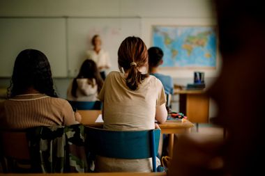 Rear view of teenage girls and boys learning in classroom