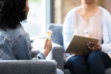 The young woman holds onto the prescription bottle while she listens to the doctor