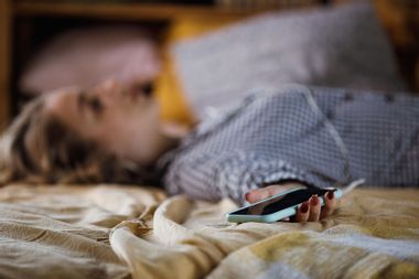 Teenage girl lying on bed holding phone