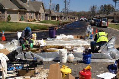 Workers scrub crude oil from their boots in the Northwoods subdivision where an ExxonMobil pipeline ruptured in Mayflower