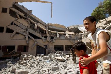 Boy looks after his brother as they walk near wreckage of school Libyan officials say was bombed by NATO forces in Zlitan