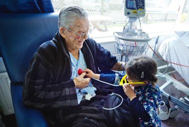 Small girl measuring heart beats to her sick grandfather with a toy stethoscope
