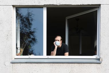 Man wearing a face mask looking out of a window