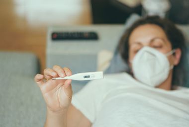 Woman Holding Thermometer While Lying On Bed