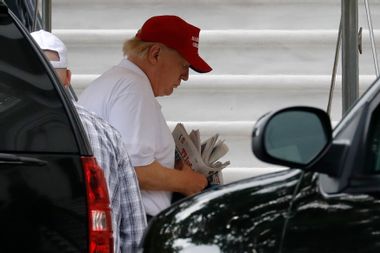 Former President Donald Trump thumbs through a stack of newspapers.
