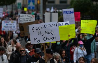 Anti-vaccine protesters hold signs, including one which reads "Freedom! My body, my choice."