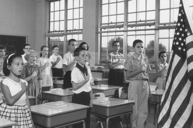 School children holding their hands over their hearts while reciting the Pledge of Allegiance in a classroom.