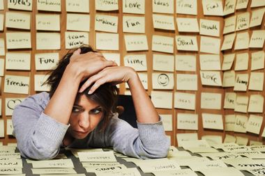 Woman at desk surrounded in adhesive notes, head in hands