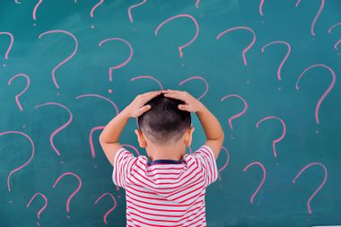 A little boy in front of blackboard with question marks
