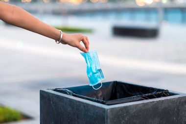 Woman throwing protective surgical mask into the garbage bin