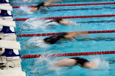 Motion view of girl backstroke swimmers starting a race and entering the water together