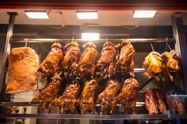 Roast duck, crispy pork belly and barbecue pork displayed in front of a Chinese restaurant
