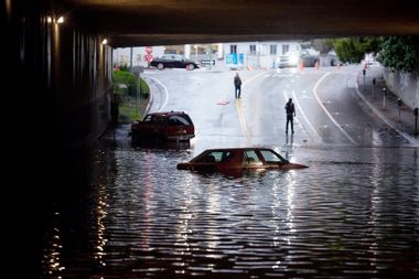 People photograph a car sitting in flooded water at an underpass