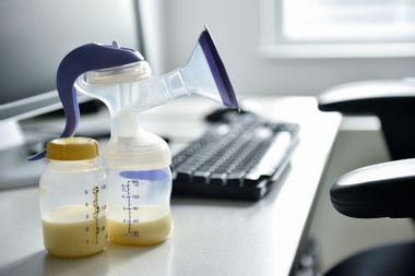 Breast pump and bottle of breast milk near computer