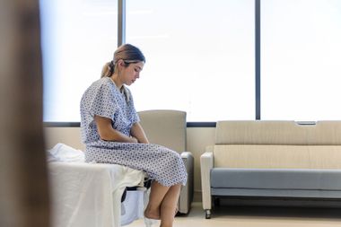 The anxious, sad, young female patient wears her gown as she waits in the hospital room