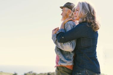 Side view of mature woman embracing man from behind against clear sky