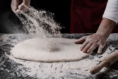 Chef spreading flour on pizza dough