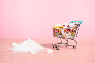 Supermarket trolley with candy next to pile of sugar