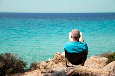 Happy senior man reading next to the Aegean sea