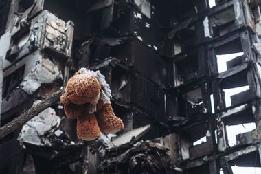 Teddy bear hanging from a tree in front of a bombed building; Ukraine; Bucha