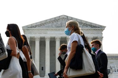A group of people wear face masks as they walk past the U.S. Supreme Court Building on June 29, 2023 in Washington, DC.