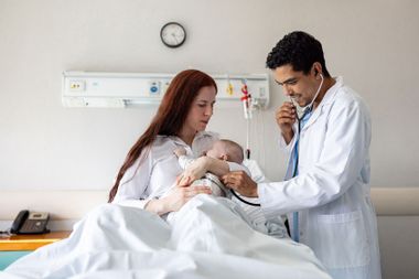 Doctor examining a newborn baby at a maternity hospital and listening to his heartbeat