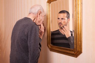 Elder man looking at an younger self in the mirror