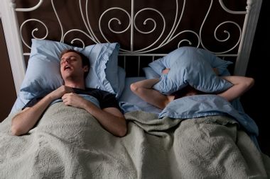Young man snoring and woman covering face with pillow