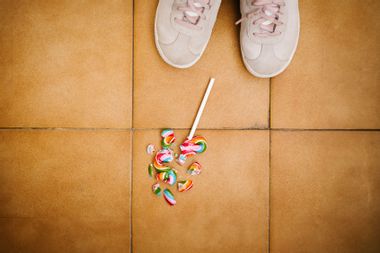 A child looks down at her broken lollipop on the floor