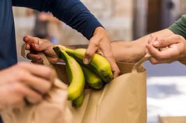 Fruit vendor helps customer stuff bananas into a paper bag