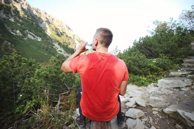 Man after trekking with sweaty t-shirt drinking water against mountains