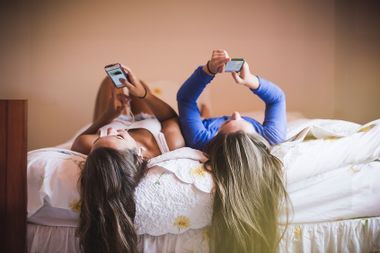 Teenage girls lying on bed looking at smart phones