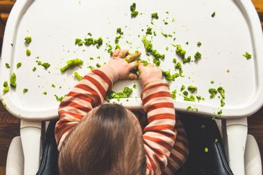 Toddler eating broccoli in high chair