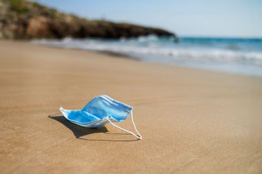 Used surgical mask thrown on the sand of a beach