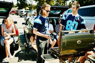 Smiling friends wearing team jerseys barbecuing at tailgating party in football stadium parking lot