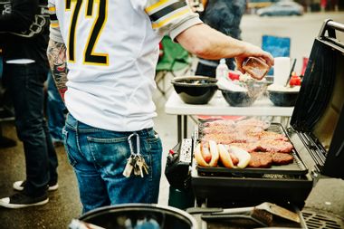Man seasoning burgers on grill at tailgating party